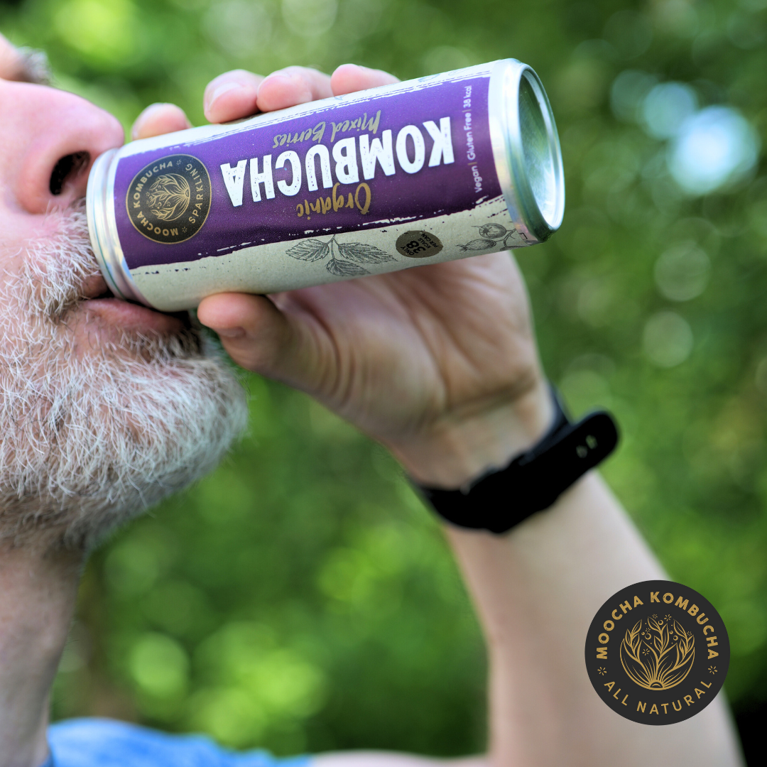 a man with a beard drinking from a can of moocha kombuhca, his had is on the can raising it up to his mouth and drinking it
