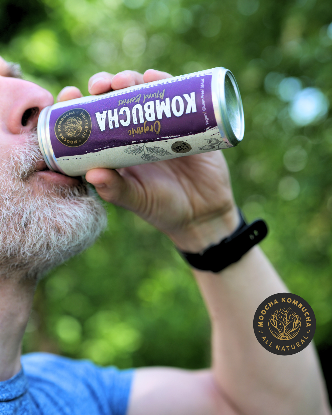 a man with a beard drinking from a can of moocha kombuhca, his had is on the can raising it up to his mouth and drinking it